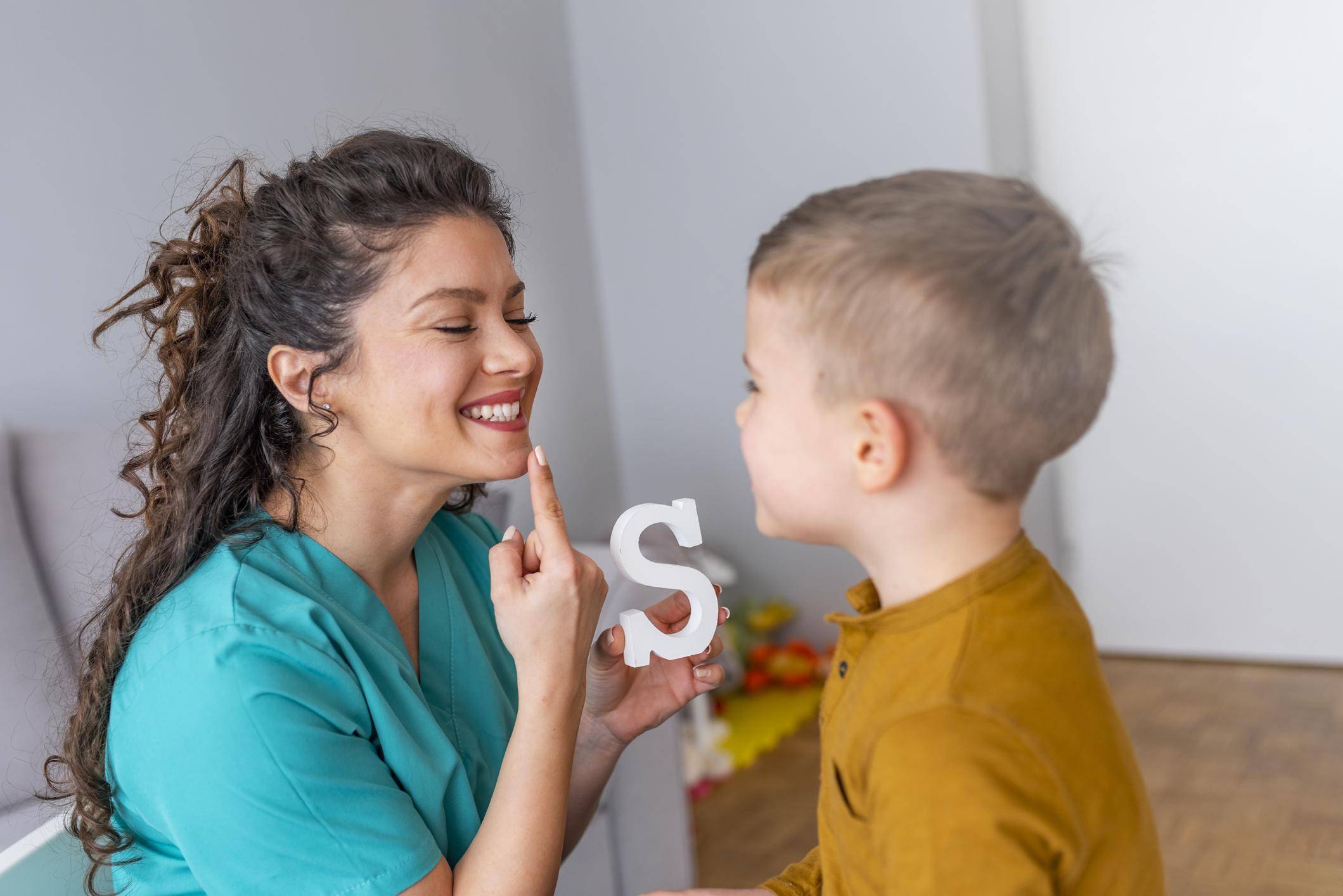 Shot of a speech therapist during a session with a little boy Cute little boy at speech therapist office. Shot of a speech therapist during a session with a little boy. Boy and young woman teacher during private home lesson